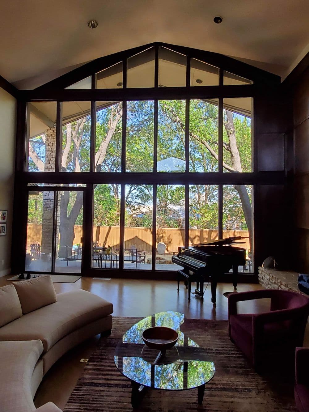 Modern living room with large windows, grand piano, and stylish furniture, overlooking natural scenery.