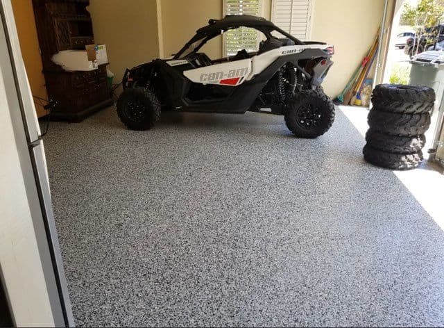 Can-Am off-road vehicle parked on a speckled garage floor with tires stacked nearby.